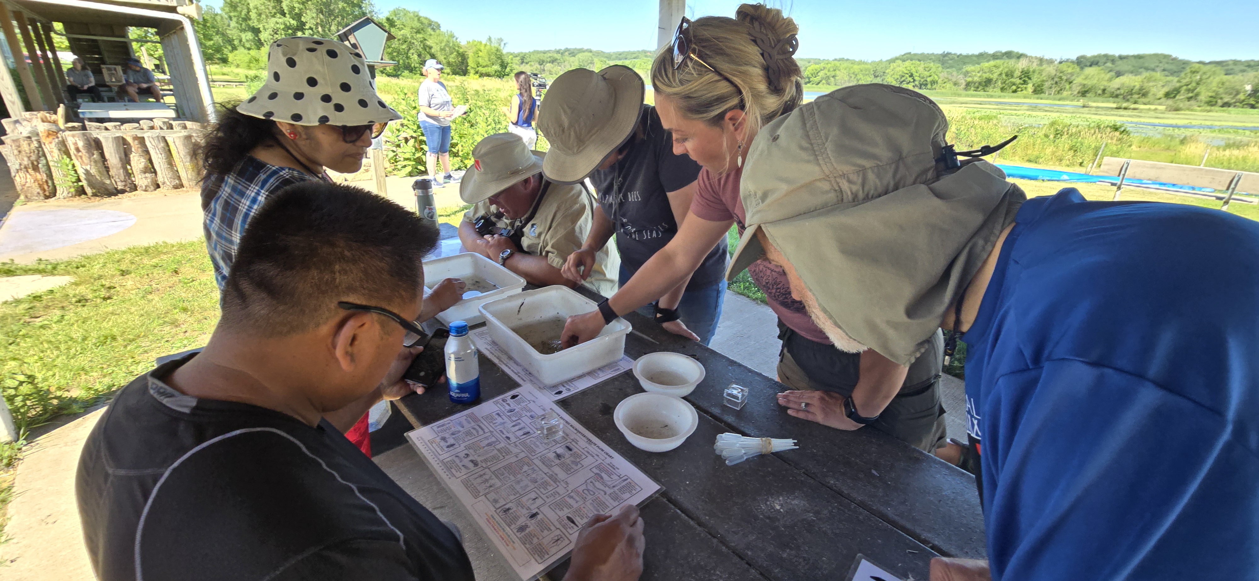 Several people looking at water specimens on a picnic table