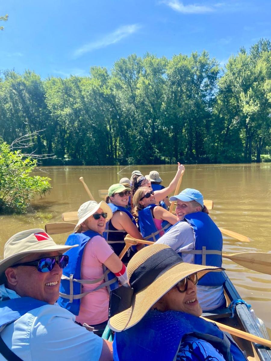 Several adults in a canoe on the water looking over their shoulders and smiling at the camera