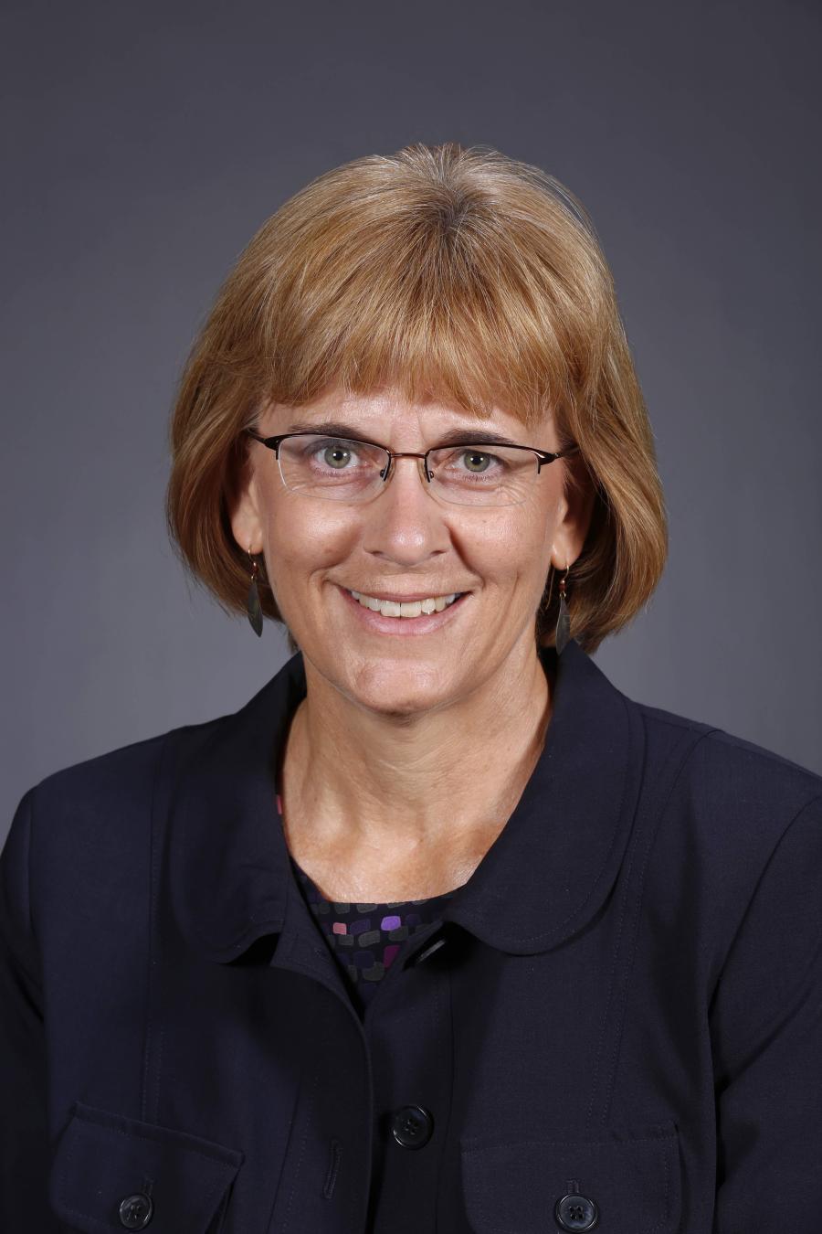 Diane Rover - smiling woman with bobbed red hair, glasses, and wearing a dark blazer